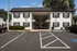 Charming white two-story apartment building with lush greenery, spacious parking, and serene surroundings.