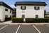Charming white two-story apartment building with lush greenery, spacious parking, and serene surroundings.
