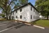 Charming white two-story apartment building with lush greenery, spacious parking, and serene surroundings.