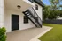 Inviting apartment entryway with sleek black stairs, elegant modern door, and spacious patio leading to a lush green lawn.