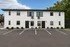 Contemporary white apartment building with black trim and ample parking space, set against a clear blue sky.