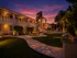 Charming apartment complex at sunset with lush greenery, palm trees, and warm exterior lighting creating a welcoming atmosphere.