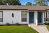 Charming duplex with dual blue doors, manicured lawns, and inviting windows, surrounded by lush greenery.