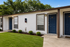 Charming apartment entrance with fresh white facade, blue doors, and lush green lawn.