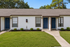 Charming duplex with crisp white facade and inviting blue doors, surrounded by lush green lawn, perfect for comfortable living.