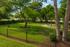 Lush green park with shady trees, benches, and a fenced area perfect for relaxing outdoor activities.