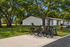 Charming apartment complex surrounded by lush greenery, featuring a bike rack and serene outdoor seating under large trees.