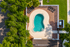 Aerial view of a luxurious backyard with a uniquely shaped swimming pool, surrounded by elegant patio furniture, vibrant greenery, and a brick-paved lounging area.
