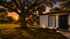 Charming home exterior bathed in sunset glow, featuring a lush lawn, majestic oak tree, and tranquil pond with fountain.