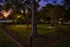 Charming fenced park area with a sunset backdrop, lush greenery, mature trees, and a cozy bench perfect for relaxation.