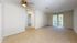 Bright and spacious living room with large windows, plush carpeting, and modern ceiling fan, perfect for comfortable living.