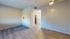 Bright, modern apartment room with stylish wooden flooring and soft lighting, featuring an open doorway leading to a cozy kitchen.