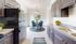 Bright and modern kitchen with sleek countertops, dark cabinetry, stainless steel sink, and adjacent dining area with elegant blue chairs and a stylish round table.