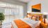Bright and modern bedroom with floor-to-ceiling windows, vibrant orange accents, and stylish wooden furniture.