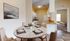 Inviting dining area with elegant marble table set for four, adjacent to a modern kitchen with white cabinetry. Cozy living space visible through an open doorway.