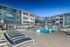 Modern luxury apartment complex featuring a pristine outdoor pool, surrounded by comfortable lounge chairs, set against a vibrant blue sky backdrop.