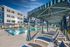 Luxurious apartment complex with a pristine swimming pool, surrounded by stylish cabanas and modern architecture under a clear blue sky.