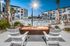 Luxurious apartment complex pool area at dusk with cozy fire pit, inviting white chairs, and modern amenities surrounded by palm trees.