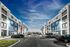 Chic modern apartment complex with vibrant blue and white exterior, surrounded by lush greenery and ample parking space, under a stunning blue sky.