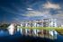 Elegant waterfront apartment complex under a stunning night sky, featuring modern architecture and serene water reflections.
