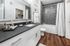 Modern bathroom with elegant gray tile backsplash, sleek white vanity, and polished wood flooring.