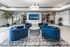 Modern living area with stylish blue armchairs, sleek coffee table, and elegant lighting, accentuated by a large wall-mounted TV and contemporary decor.