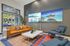Contemporary living room with a sleek design, featuring a tan leather sofa, modern armchairs, vibrant rug, and stunning nature images on wall displays.