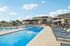 Luxurious apartment complex with a pristine outdoor swimming pool, sun loungers, and shaded seating area, surrounded by lush greenery and modern architecture.