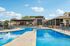 Inviting outdoor pool area with modern lounge chairs, a covered patio, and a stylish clubhouse under a clear blue sky.