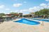 Inviting apartment complex with a luxurious outdoor pool, surrounded by stylish lounge chairs and vibrant greenery under a clear blue sky.