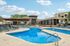 Luxurious apartment complex showcasing a sparkling swimming pool, stylish lounge chairs, and modern clubhouse under a bright blue sky.