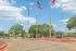 Inviting residential entrance with three flagpoles, vibrant landscaping, and charming brick buildings set against a clear blue sky.