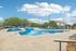 Inviting outdoor pool area with stylish lounge chairs and lush landscaping, perfect for relaxation under a beautiful blue sky.