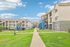 Charming apartment complex with modern architecture, featuring spacious balconies and lush green lawns under a clear blue sky.