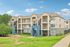 Charming multi-story apartment building with elegant architecture, surrounded by lush greenery and a clear blue sky.