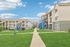 Charming apartment complex with modern two-story buildings set amidst lush green lawns and blue skies.