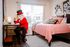 Charming bedroom with a cozy pink bedspread, decorative pillows, a bright window view, and a whimsical character in a red jacket at a sleek desk.