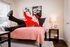 Charming bedroom with a playful mascot pose, featuring a cozy pink bedspread, modern decor, and soft natural lighting.