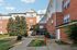 Charming red-brick apartment building surrounded by lush greenery, offering a welcoming pathway to a cozy entrance beneath clear blue skies.