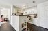 Modern open-concept kitchen with sleek white cabinets, cozy dog bed, and a charming peek into a tastefully decorated bedroom.