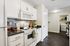 Modern kitchen with sleek white cabinetry and dark countertops, complemented by stylish tile backsplash and stainless steel appliances, leading to a convenient laundry area.