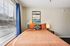 Bright and inviting bedroom with an orange bedspread, modern art, and abundant natural light from large windows.