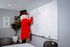 Cheerful mascot in a bright red coat writing on a whiteboard in a modern conference room.