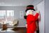 Bright apartment living space with a large window, elegant armchair, and unique decor. A fun character in a vibrant red outfit adds charm while writing on a whiteboard.