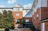 Charming brick apartment building with lush greenery and a welcoming entrance, under a bright blue sky.