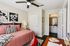 Bright and airy bedroom featuring elegant ceiling fan, cozy bed with soft pink quilt, decorative floral artwork, and inviting entrance to a modern en-suite bathroom.