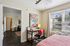 Charming and sunlit bedroom with stylish workspace, featuring a vibrant floral painting, modern desk, and large window with serene outdoor views.