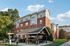 Charming brick apartment building with outdoor seating area, nestled in lush greenery under a bright blue sky.