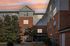 Charming brick apartment building at sunset, featuring large windows and surrounded by lush greenery.
