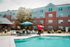 Charming brick apartment complex with inviting poolside seating, lush greenery, and vibrant outdoor atmosphere perfect for relaxation.
